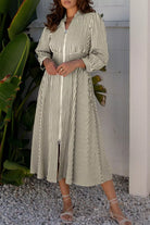 NEWYORKLISTED STYLE COLLECTION: Woman wearing a striped dress standing outdoors with plants and a white wall in the background