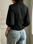 NEWYORKLISTED STYLE COLLECTION: A woman shown from the back wearing a black puff-sleeve collared blouse tucked into light-wash blue jeans with decorative bow embroidery on the back pockets.