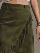 NEWYORKLISTED STYLE COLLECTION: An olive green suede skirt with long fringe trim, shown on a model. The skirt features an asymmetrical design with a side pocket and a belt loop.