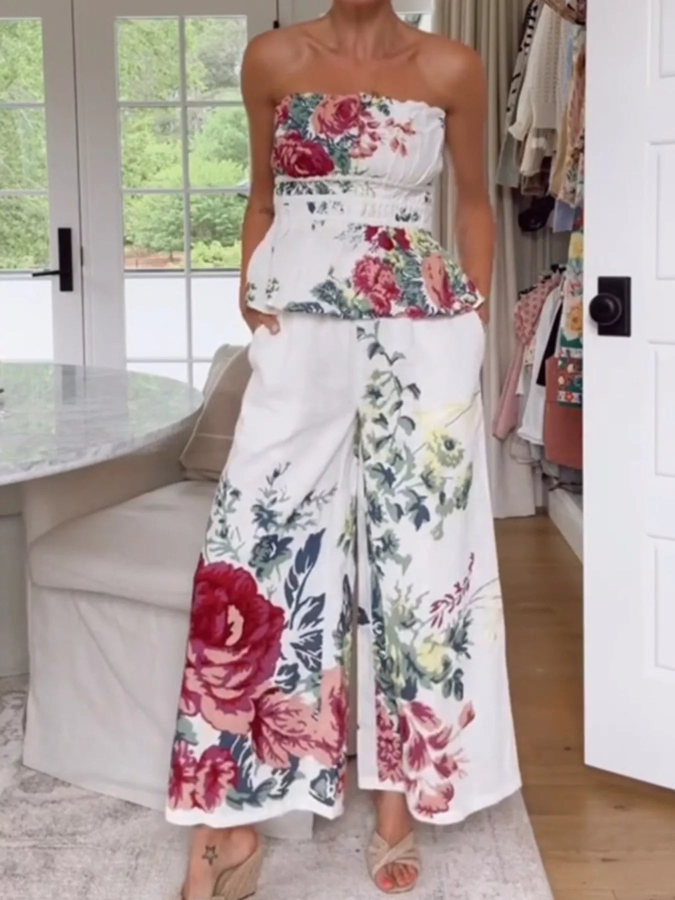 NEWYORKLISTED STYLE COLLECTION: Woman wearing a floral strapless top and wide-leg pants in a room with a door open to another room.