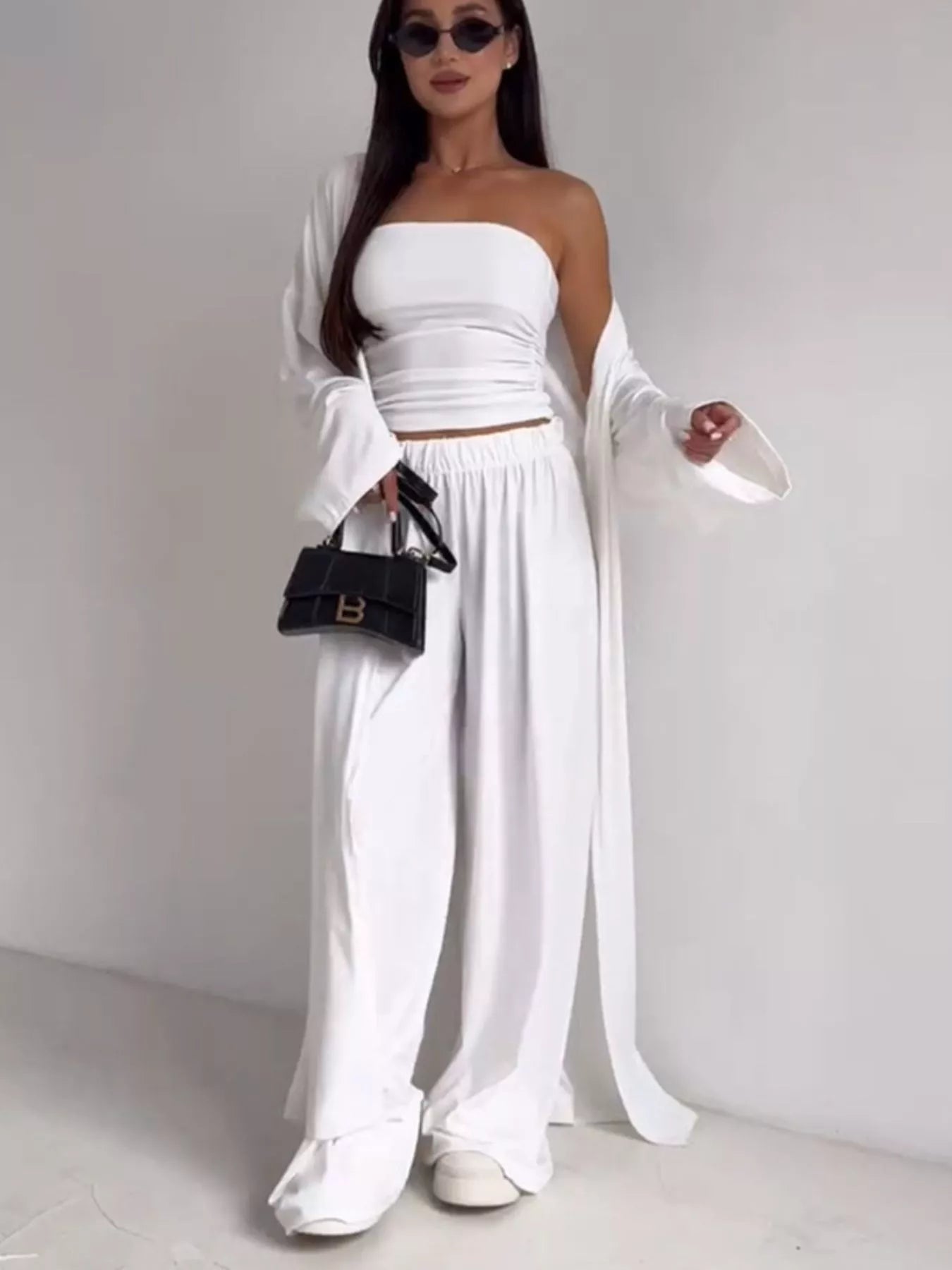 NEWYORKLISTED COMFORT COLLECTION: Woman wearing a white outfit with a black handbag on a plain background