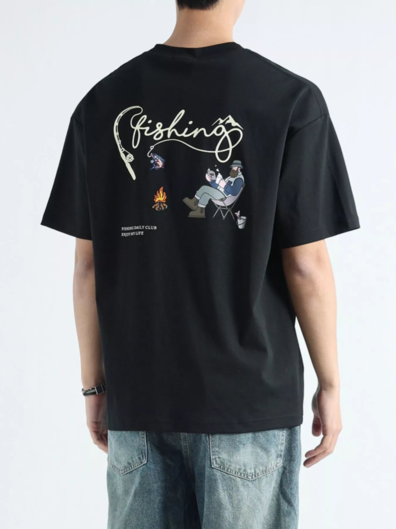 Person wearing a black t-shirt with fishing-themed graphics on the back, standing against a light gray background.