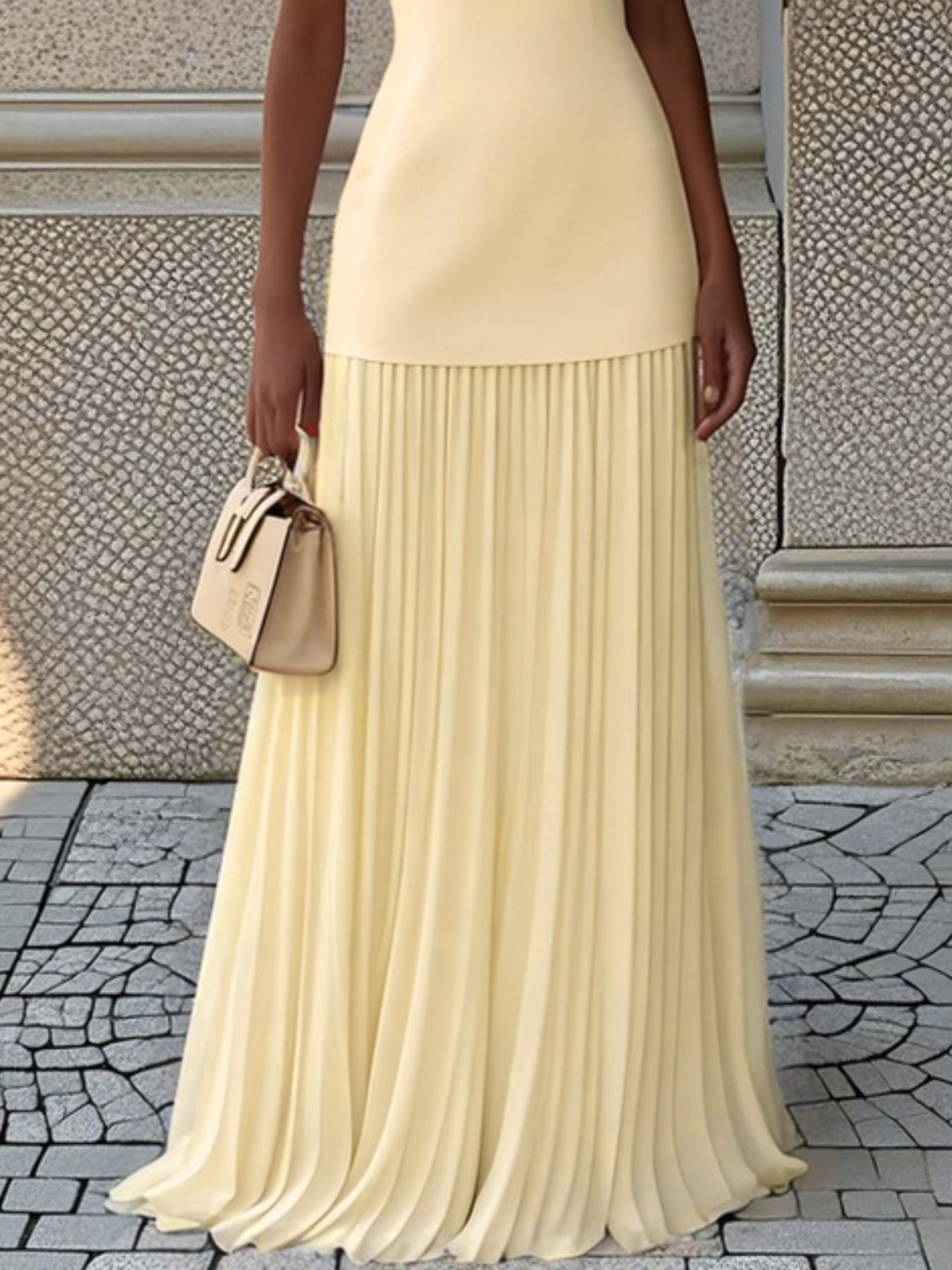 NEWYORKLISTED STYLE COLLECTION: Person wearing a beige pleated skirt and holding a matching handbag on a stone pavement.
