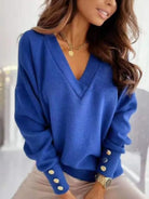 NEWYORKLISTED STYLE COLLECTION: A woman wearing a royal blue V-neck knit sweater with decorative gold-tone buttons on the cuffs, paired with light beige pants and a gold necklace.