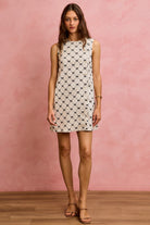 NEWYORKLISTED STYLE COLLECTION: Woman wearing a sleeveless dress with a pattern against a pink wall.