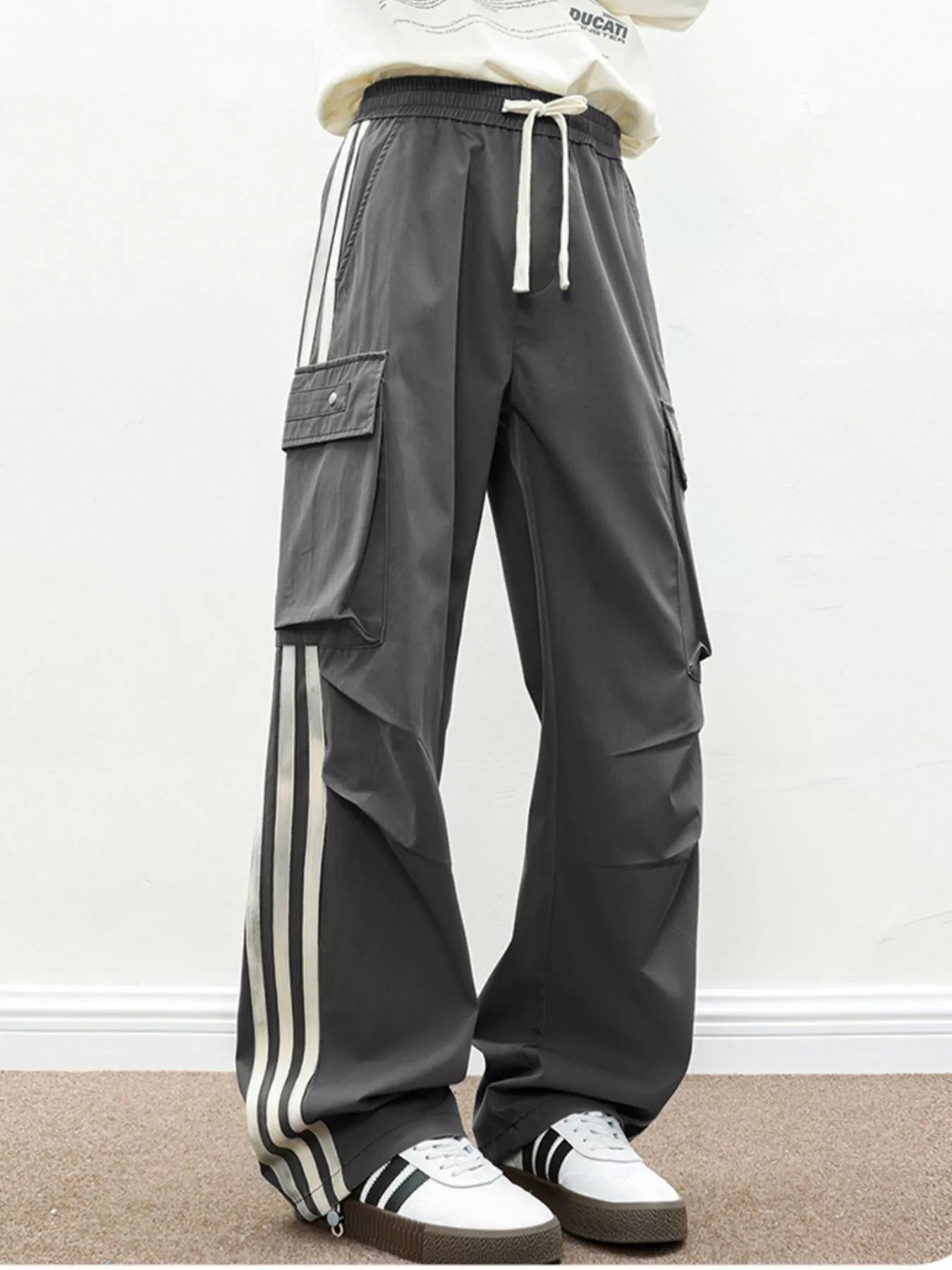 NEWYORKLISTED ATLAS MEN's COLLECTION: Person wearing gray cargo pants with white stripes and white sneakers on a plain background