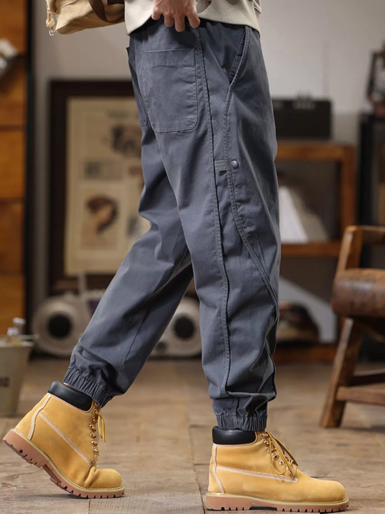 NEWYORKLISTED ATLAS MEN's COLLECTION: Person wearing gray cargo pants and yellow boots in a room with furniture and decor.