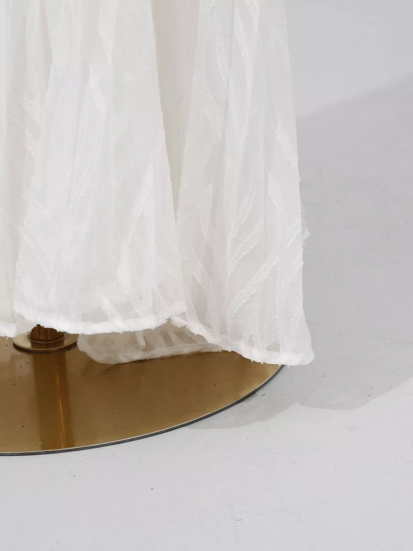 NEWYORKLISTED STYLE COLLECTION: White sheer fabric draped over a gold circular object on a white background