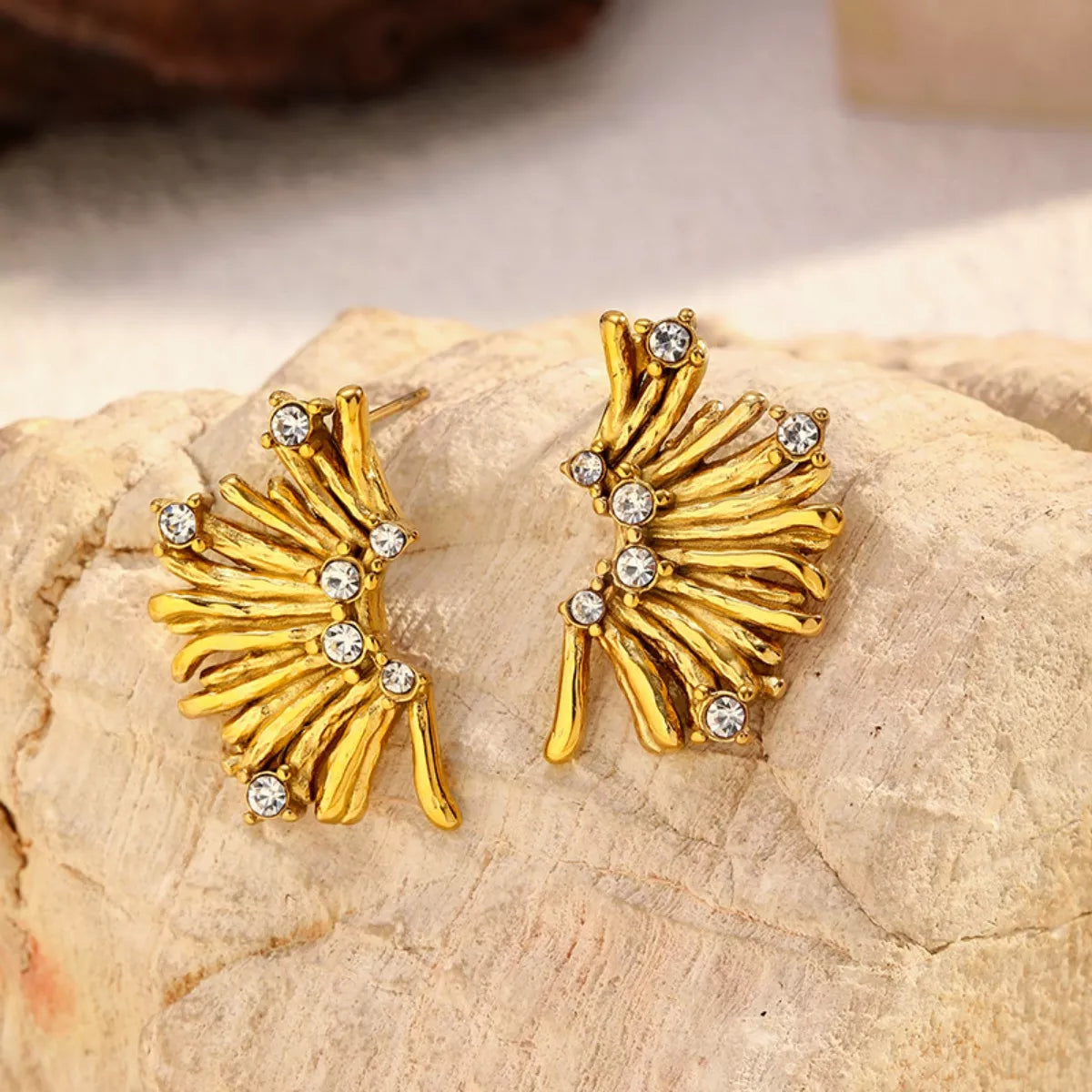 NYLD Glamour Collection by NEWYORKLISTED: Gold earrings with gemstones on a stone surface