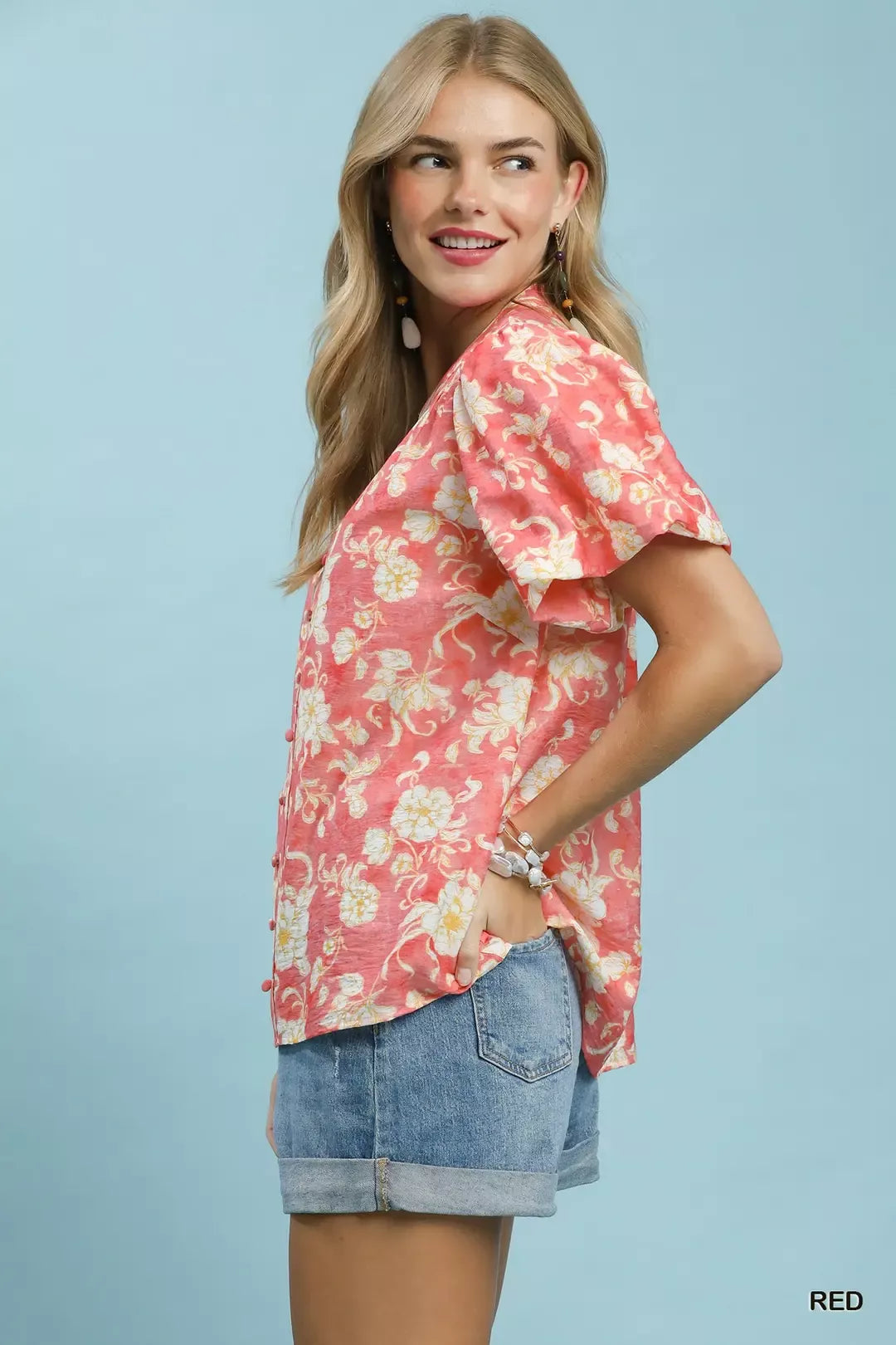 NEWYORKLISTED STYLE COLLECTION: Woman wearing a pink floral blouse and denim shorts against a light blue background