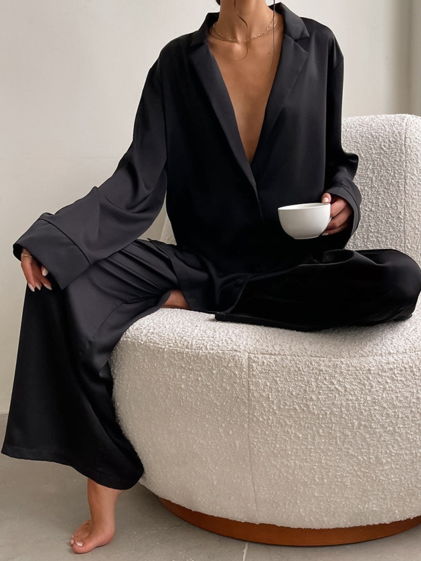 NEWYORKLISTED Intimate Apparel Collection: Person wearing a black outfit sitting on a textured ottoman holding a white cup.