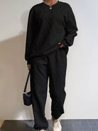 NEWYORKLISTED COMFORT COLLECTION: Person wearing a black cable knit sweater and pants with a white wall background
