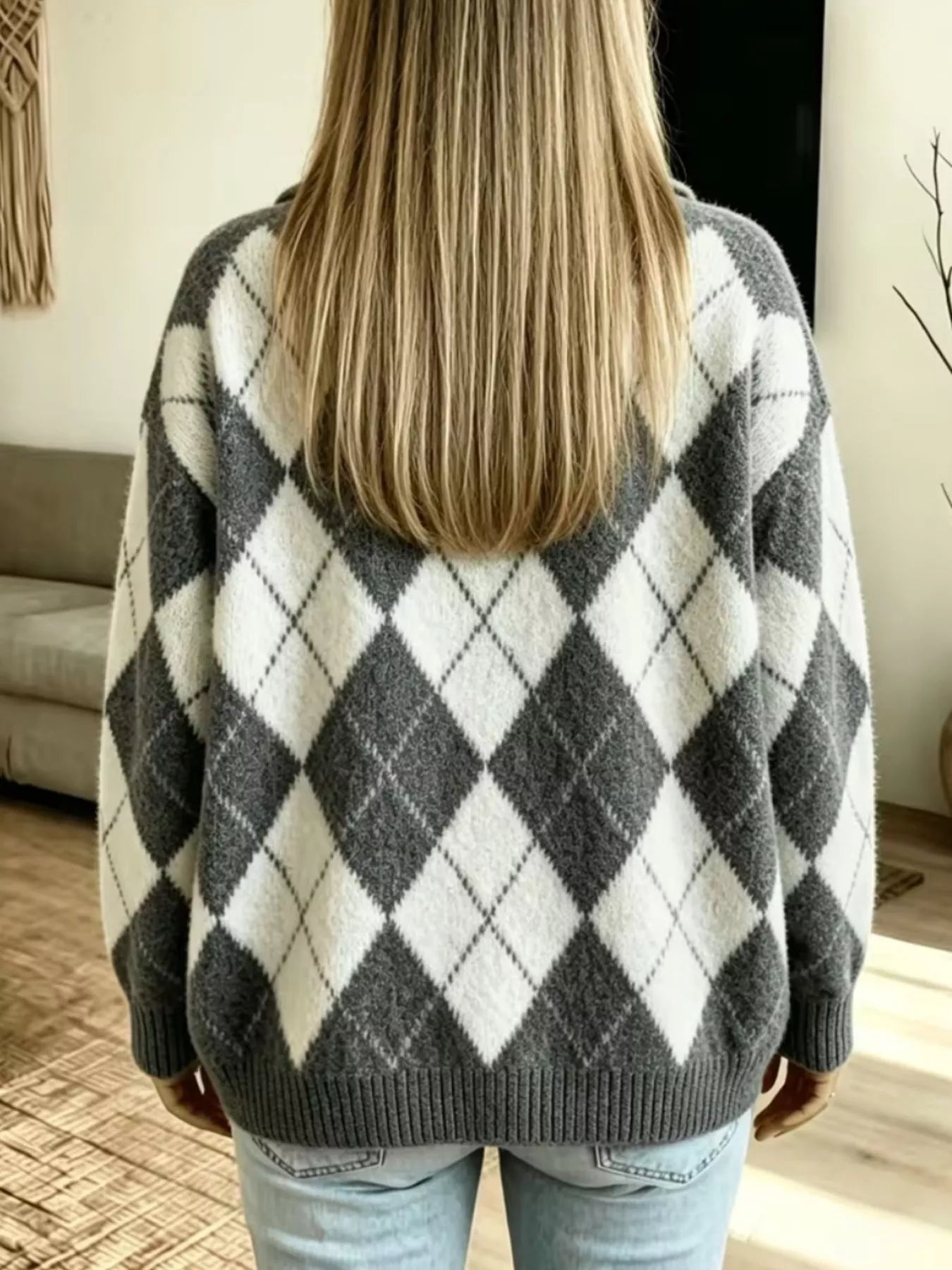 NEWYORKLISTED STYLE COLLECTION: A woman viewed from behind wearing a fuzzy knit sweater with a large gray and off-white argyle pattern, paired with light blue jeans in a home setting.