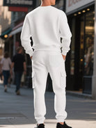 NEWYORKLISTED ATLAS MEN'S COLLECTION: A man standing on a city street, viewed from the back, wearing a matching white waffle-knit crewneck sweatshirt and cargo pants set.