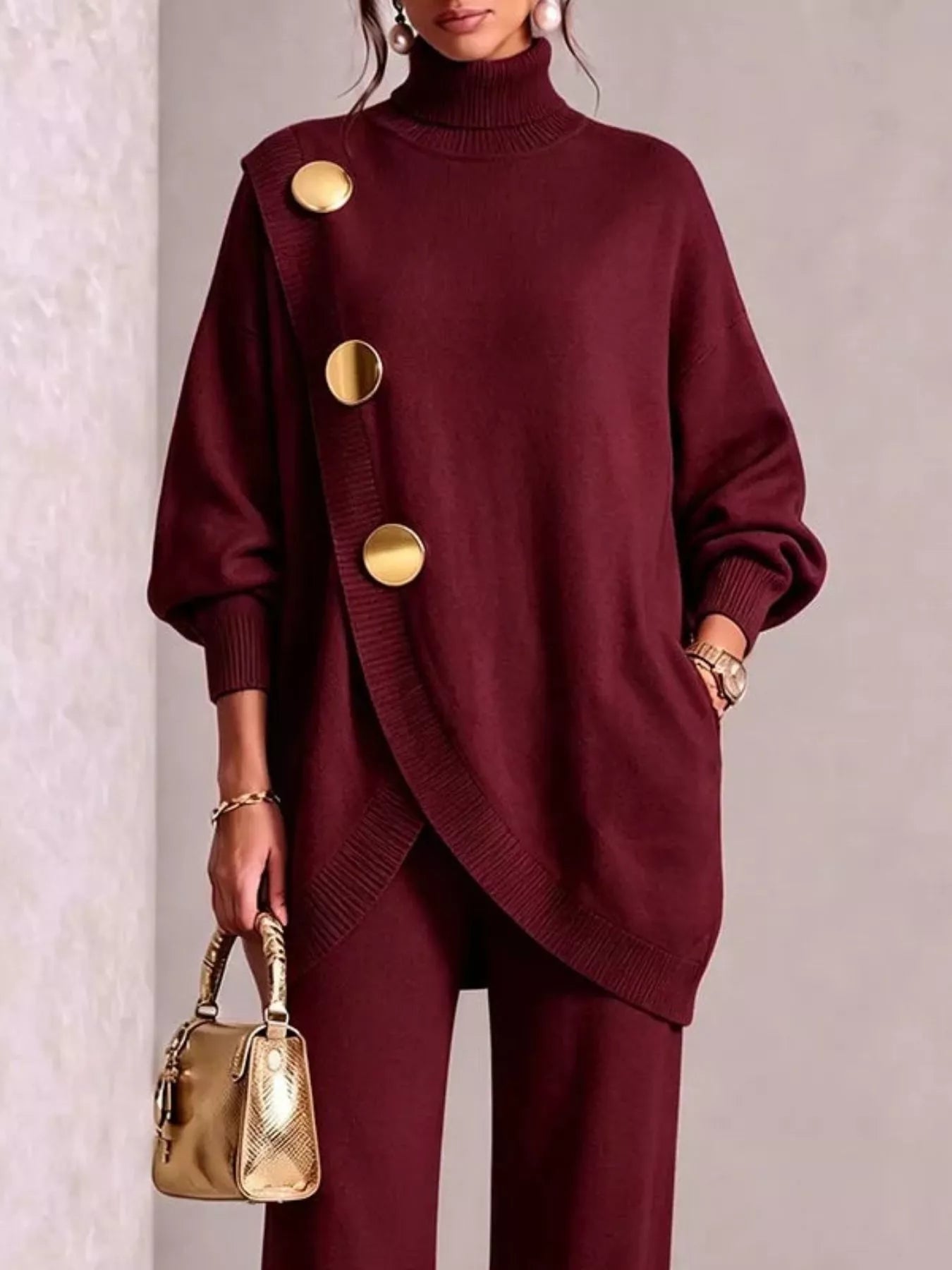 NEWYORKLISTED STYLE COLLECTION: A woman models a deep burgundy knit turtleneck sweater with oversized gold buttons and matching trousers, holding a small gold handbag against a neutral textured wall.