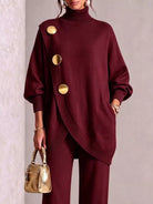 NEWYORKLISTED STYLE COLLECTION: A woman models a deep burgundy knit turtleneck sweater with oversized gold buttons and matching trousers, holding a small gold handbag against a neutral textured wall.