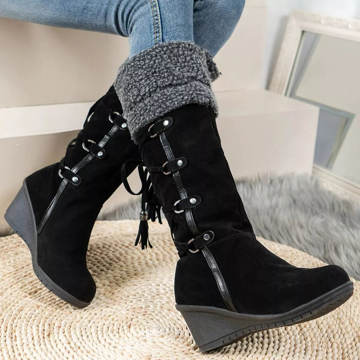 NEWYORKLISTED SHOE COLLECTION: Black lace-up boots worn with blue jeans and gray sweater cuffs, sitting on a textured surface.