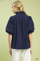 NEWYORKLISTED STYLE COLLECTION: Woman wearing a navy blue blouse with puffed sleeves on a light green background