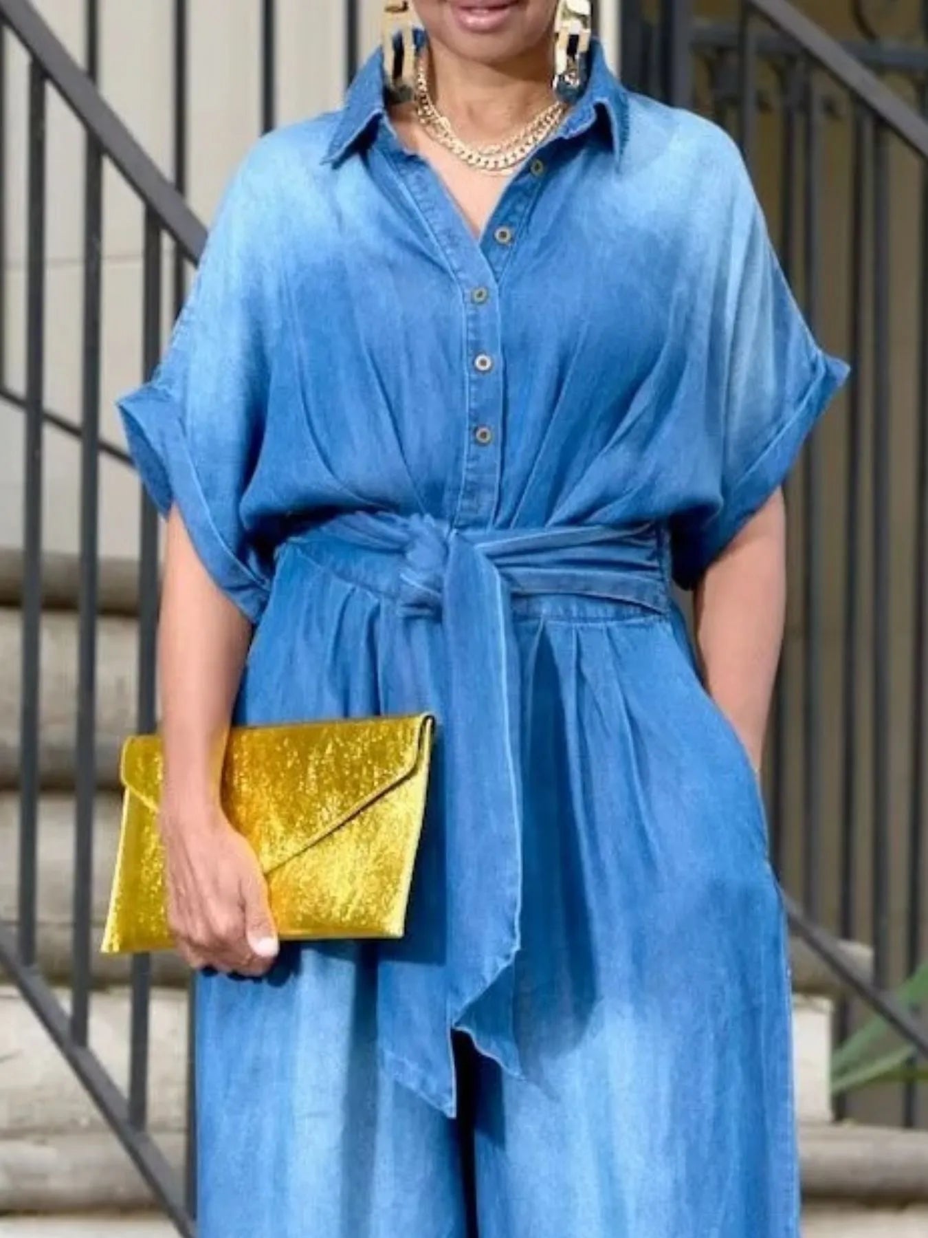 NEWYORKLISTED STYLE COLLECTION: Person wearing a blue dress holding a gold clutch against a neutral background