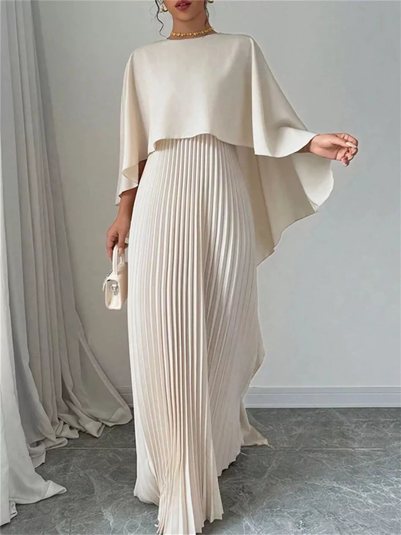 NEWYORKLISTED STYLE COLLECTION: Woman wearing a beige outfit with a draped top and pleated skirt against a plain background