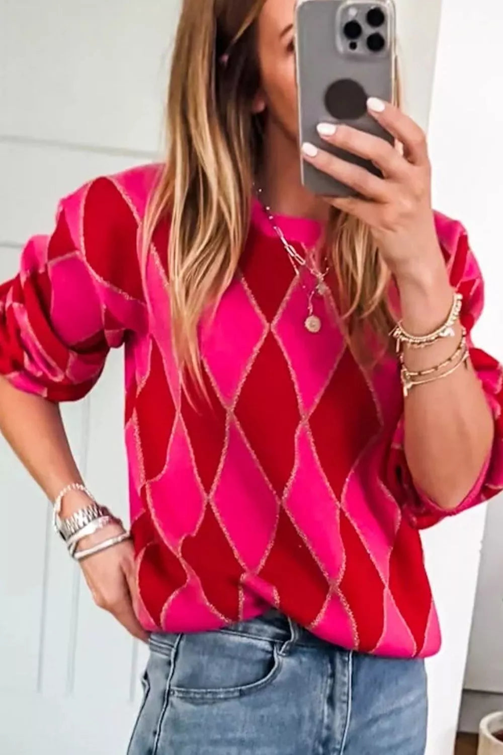 NEWYORKLISTED STYLE COLLECTION: Person wearing a pink diamond patterned top and blue jeans, taking a mirror selfie.