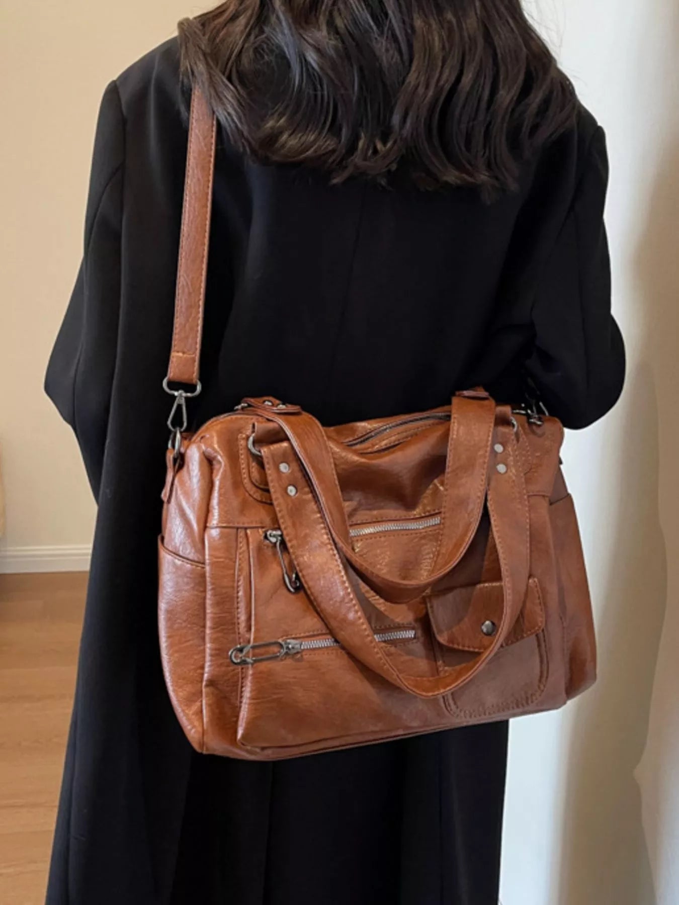 NEWYORKLISTED STYLE COLLECTION: Person wearing a brown leather handbag over one shoulder against a neutral background