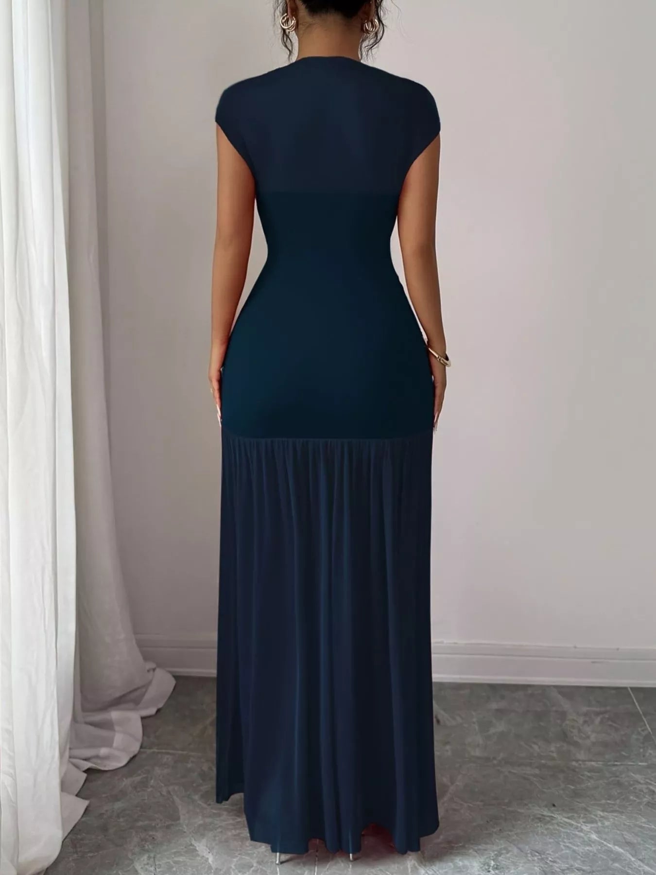 NEWYORKLISTED STYLE COLLECTION: Woman wearing a dark blue dress standing against a plain wall.