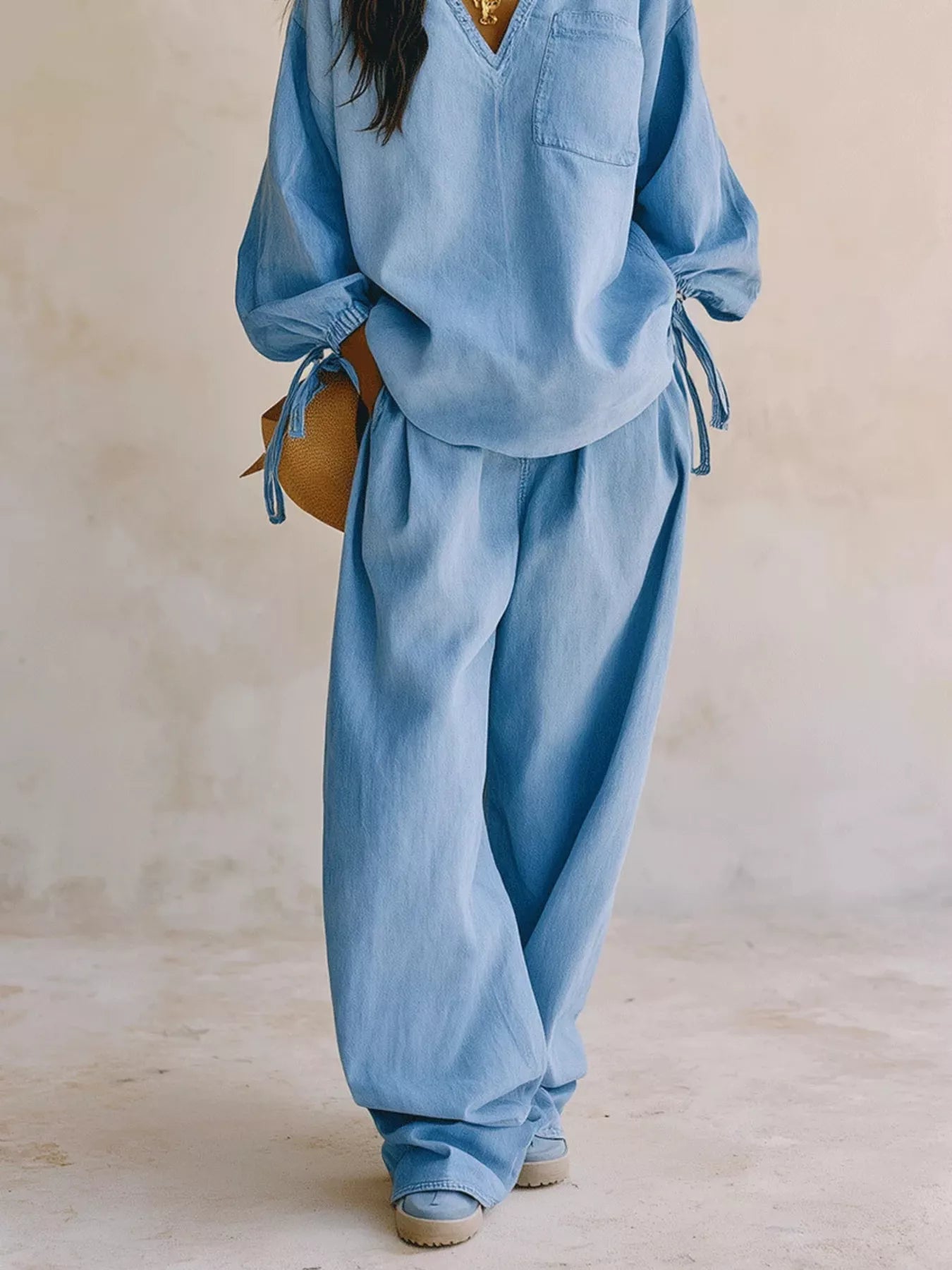 NEWYORKLISTED STYLE COLLECTION: A person wearing a light blue matching lounge set with a loose long-sleeve top and wide-leg pants, standing against a neutral beige wall.