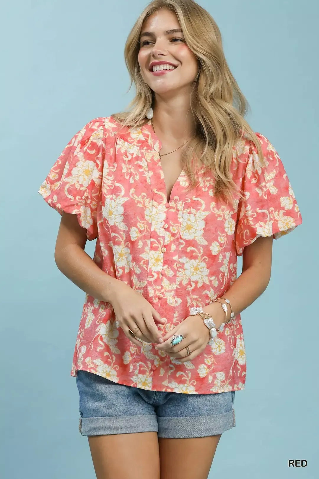 NEWYORKLISTED STYLE COLLECTION: Woman wearing a pink floral blouse and denim shorts against a light blue background