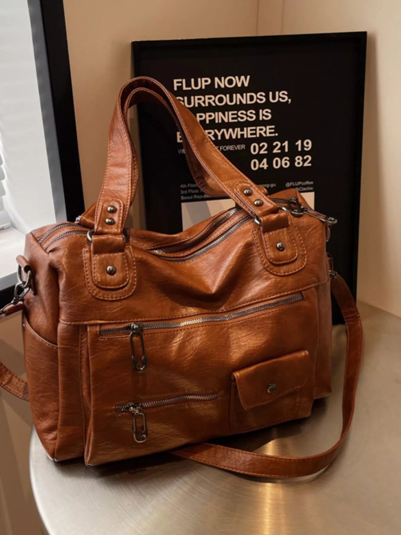 NEWYORKLISTED STYLE COLLECTION: Brown leather handbag on a reflective surface with a blurred background