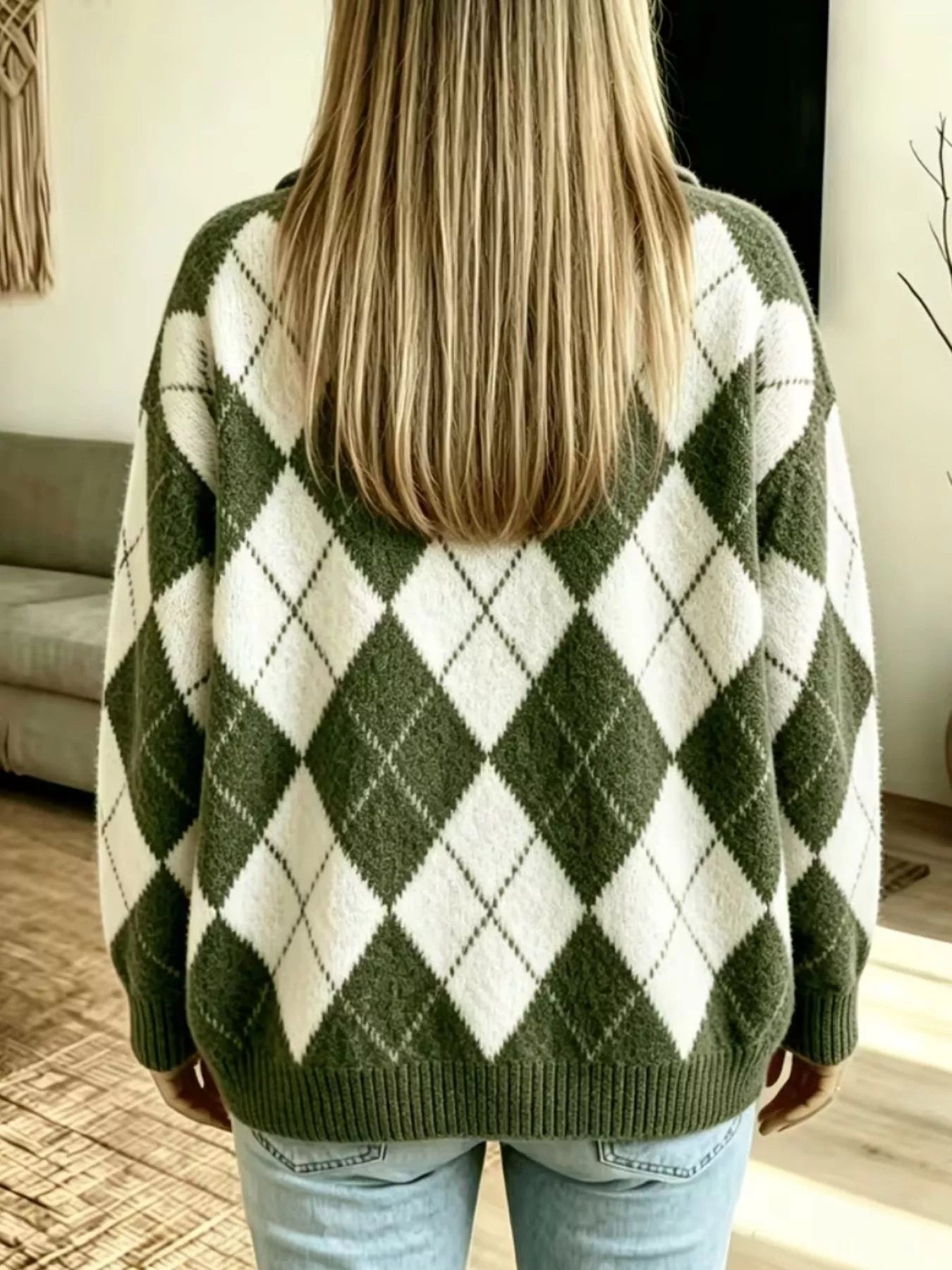 NEWYORKLISTED STYLE COLLECTION: A woman viewed from behind wearing an oversized knit sweater with an olive green and off-white argyle pattern, paired with light blue jeans in a home setting.