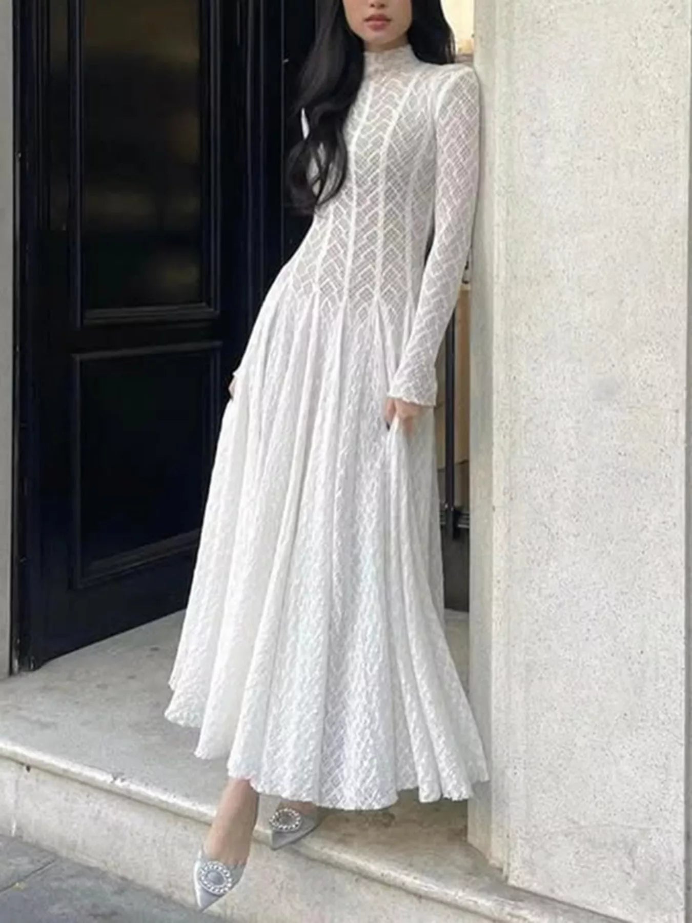 NEWYORKLISTED STYLE COLLECTION: Woman wearing a white lace dress standing against a building entrance.