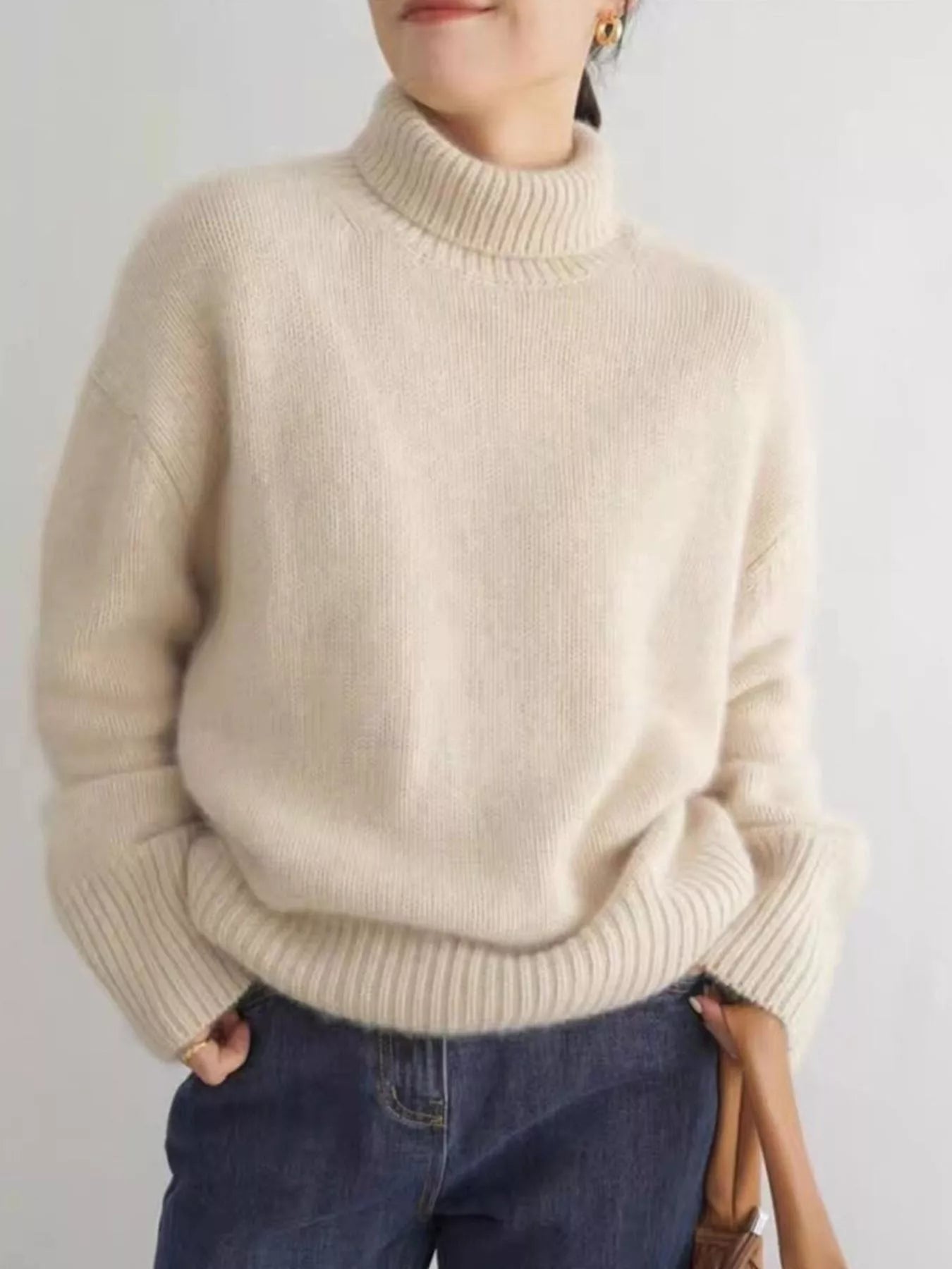 Person wearing a beige sweater and blue jeans against a plain background NEWYORKLISTED STYLE COLLECTION