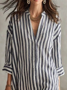 NEWYORKLISTED STYLE COLLECTION: A woman wearing a loose-fitting linen shirt dress with vertical navy and off-white stripes, styled with layered gold necklaces and earrings.