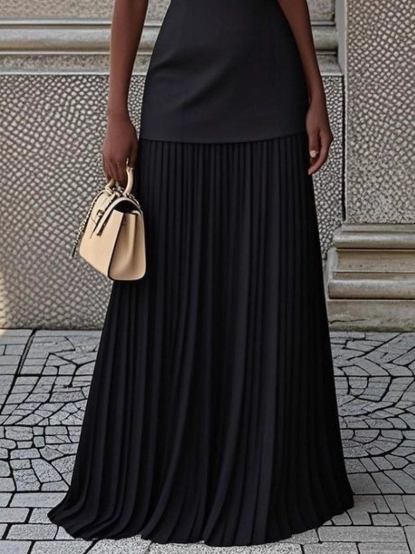 NEWYORKLISTED STYLE COLLECTION: Person wearing a black pleated skirt holding a beige handbag on a stone pavement.