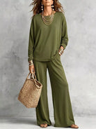 NEWYORKLISTED STYLE COLLECTION: A woman models an olive green two-piece lounge set consisting of a long-sleeve top and wide-leg pants, styled with layered gold necklaces, bracelets, and a straw tote bag against a textured gray wall.