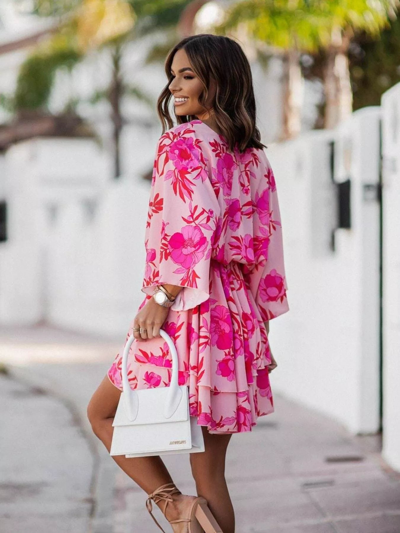 NEWYORKLISTED STYLE COLLECTION: Woman wearing a pink floral dress holding a white handbag on a street.