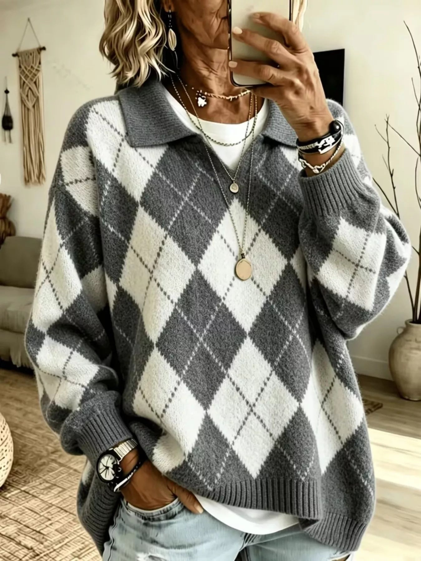 NEWYORKLISTED STYLE COLLECTION: A woman takes a mirror selfie wearing a cozy oversized knit sweater with a gray and white argyle pattern, layered over a white t-shirt and paired with light-wash jeans.