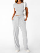 NEWYORKLISTED COMFORT COLLECTION: Woman wearing a gray crop top and pants with a white bag on a white background