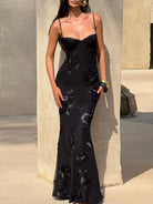 NEWYORKLISTED STYLE COLLECTION: Woman wearing a black evening gown with floral embellishments against a neutral wall.