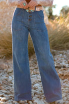 NEWYORKLISTED STYLE COLLECTION: Person wearing blue bell-bottom jeans standing on a rocky surface with a blurred natural background