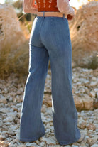NEWYORKLISTED STYLE COLLECTION: Person wearing blue flared jeans standing on a rocky surface with a blurred natural background