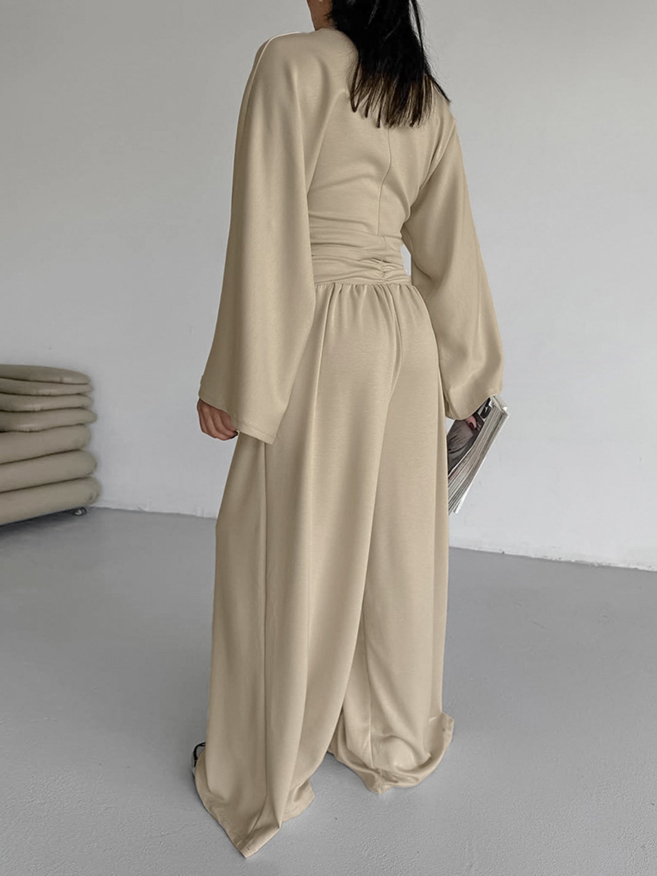 NEWYORKLISTED STYLE COLLECTION: Person wearing a beige jumpsuit in a minimalistic room.