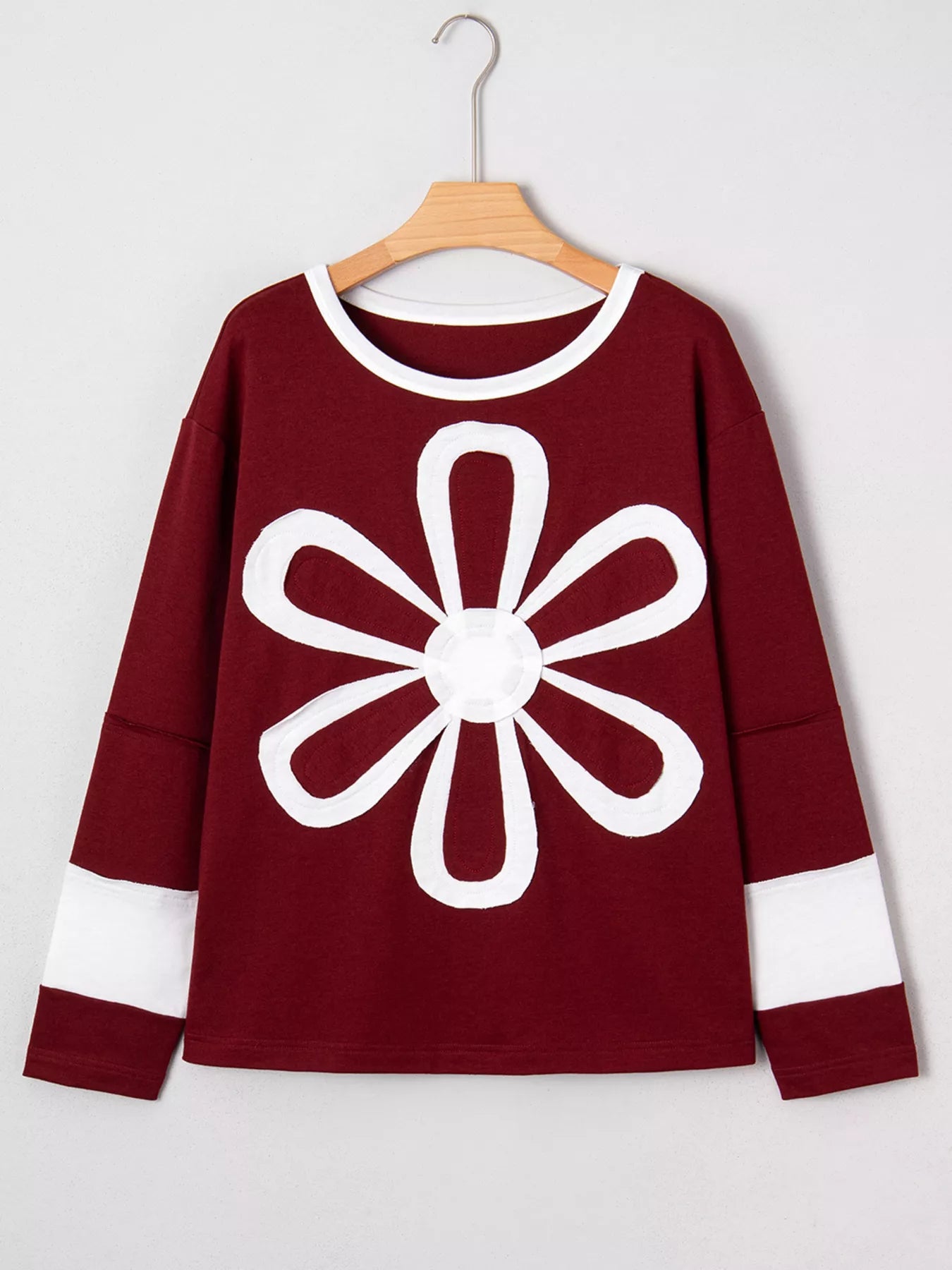 NEWYORKLISTED STYLE COLLECTION: Maroon sweater with a white flower design on a hanger against a white background