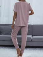 NEWYORKLISTED Intimate Apparel: Person wearing a mauve pajama set standing in a living room with a gray sofa.