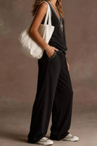 NEWYORKLISTED STYLE COLLECTION: Person wearing a black outfit with a white bag against a neutral background