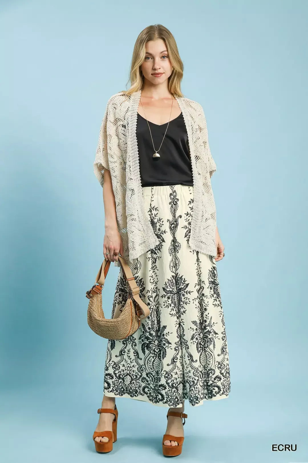 NEWYORKLISTED STYLE COLLECTION: Woman wearing a long, patterned dress with a lace cardigan against a light blue background