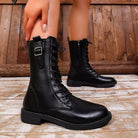 NEWYORKLISTED SHOE COLLECTION: A pair of black leather lace-up ankle boots with side buckle details, shown on a model's feet against a rustic wooden plank background.