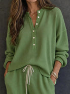 NEWYORKLISTED STYLE & COMFORT COLLECTION: A woman wearing a sage green waffle-knit long-sleeve henley top with white buttons and matching green drawstring pants, standing against a dark textured wall.