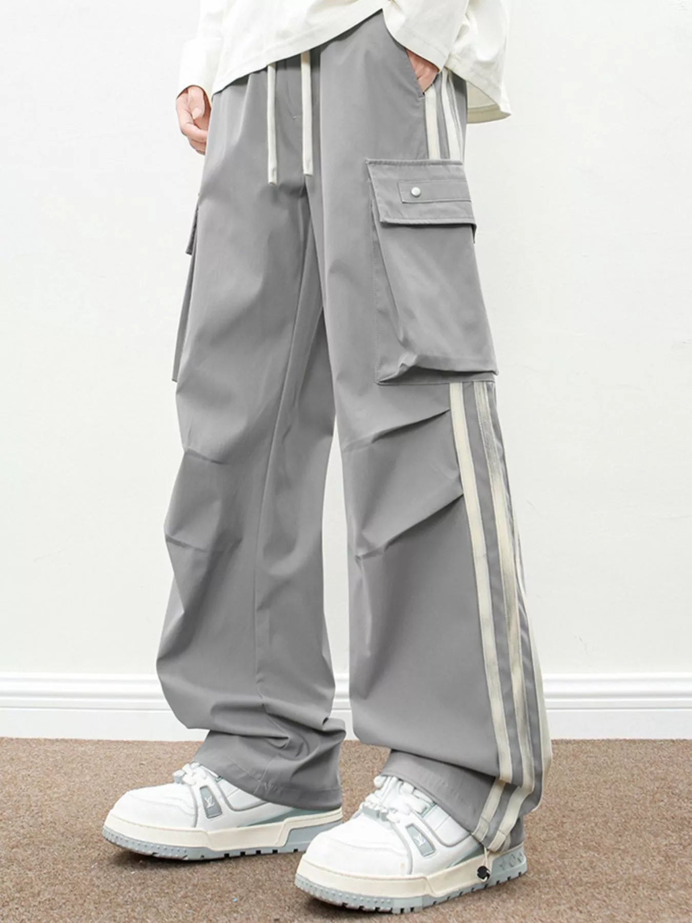 NEWYORKLISTED ATLAS MEN's COLLECTION: Person wearing gray cargo pants with white stripes and white sneakers on a plain background